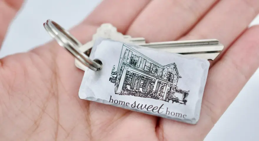 Un llavero hogar con la imagen de una casa y la frase "home sweet home" descansa en una mano.
