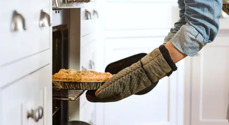 Persona saca un pastel del horno con guantes de cocina personalizados.