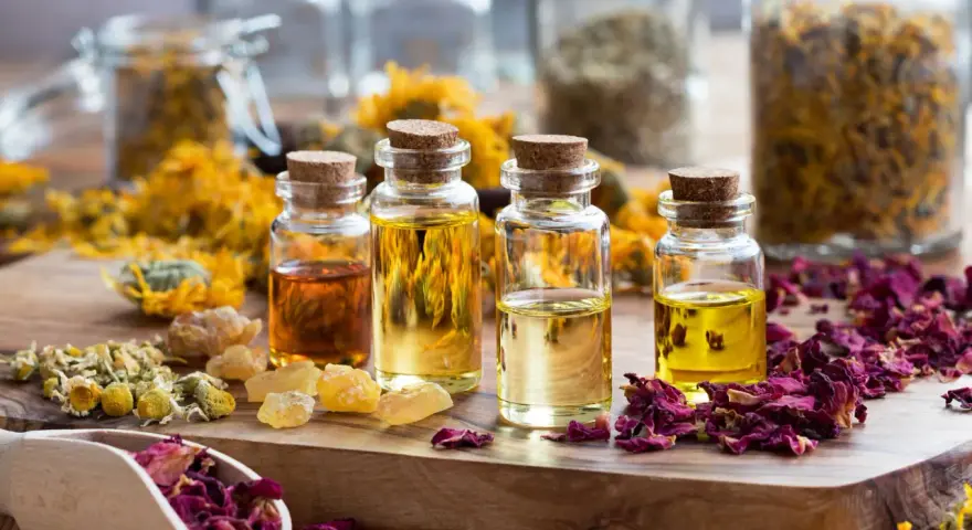 Botellas con aceites esenciales y pétalos de rosa, manzanilla y caléndula. Ideas para saber como hacer esencias aromaticas caseras.