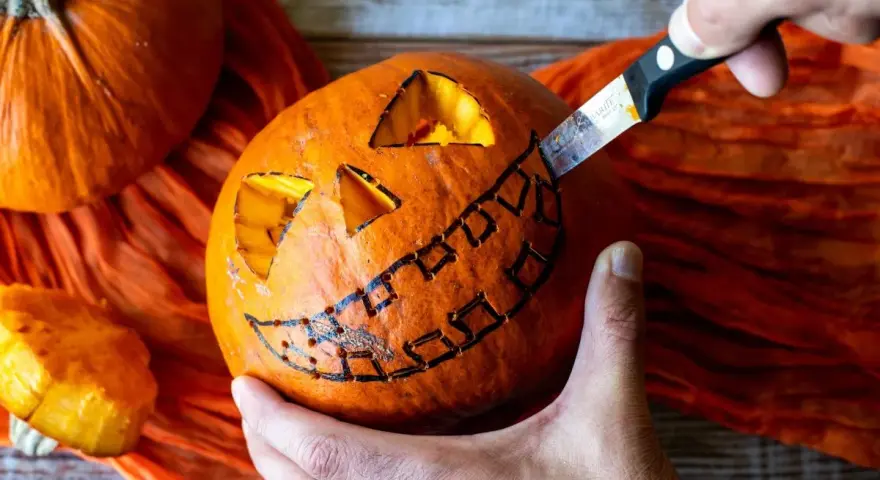 Creando una calabaza de Halloween fácil. Un cuchillo talla una sonrisa dentada en una calabaza naranja, con ojos triangulares ya cortados.