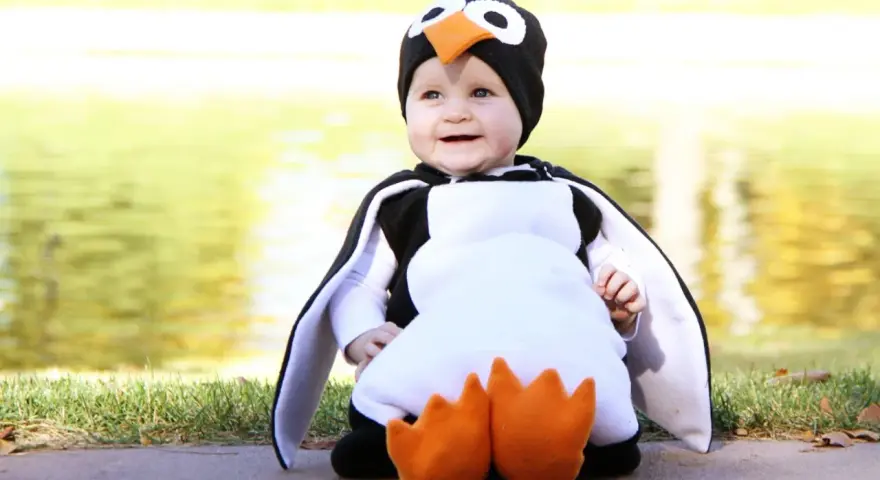 Bebé sonriente con un adorable disfraz pinguino casero, con aletas y pico naranja.