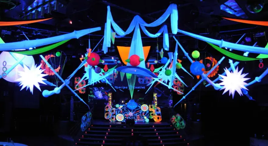 Decoración vibrante para una fiesta futurista, con luces neón, telas colgantes y estructuras geométricas que crean un ambiente de otro mundo.