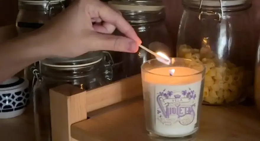 Encendiendo una vela decorada, parte de manualidades para decorar velas, con frascos de vidrio de fondo.