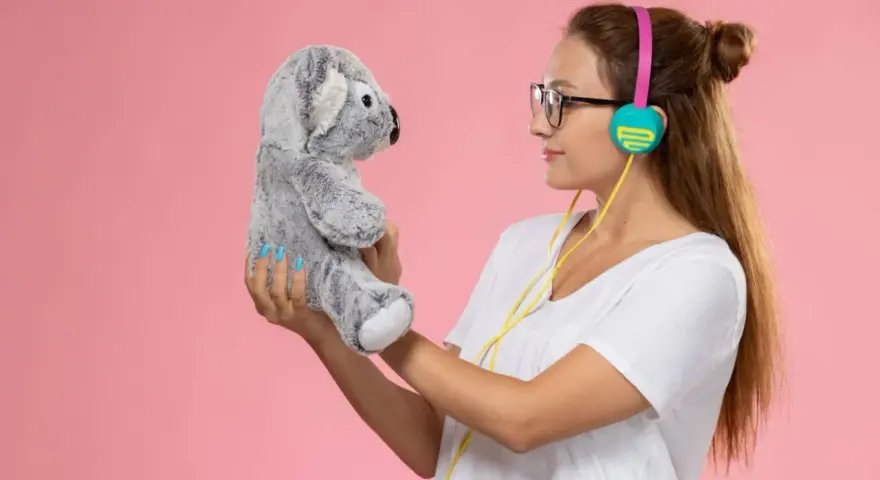 Mujer con auriculares sostiene un peluche de koala gris, como si compartieran secretos. ¡Un par de osos personalizados para la diversión!