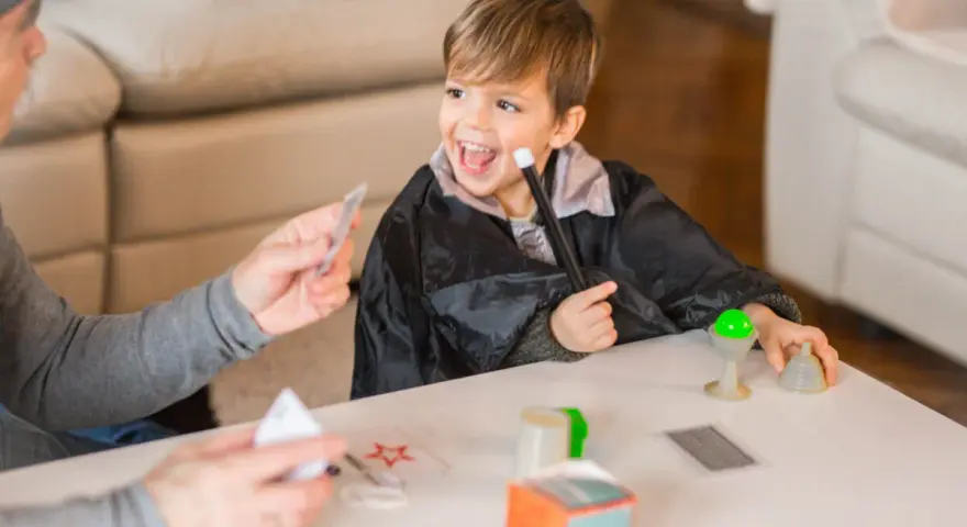 Niño con túnica de mago practica trucos de magia para niños con las manos, usando varita y cartas.