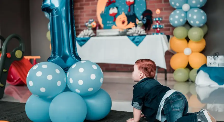 Niño gateando junto a globos azules y un gran número 1. Ideas para como preparar una fiesta infantil barata y muy original.