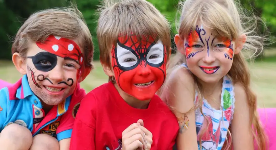 Niños con pintacaras de pirata, Spider-Man y mariposa sonriendo.