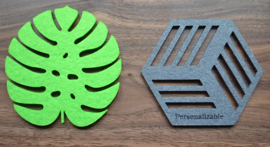 Posavasos de fieltro verde con forma de hoja y otro gris hexagonal con líneas, sobre fondo de madera.