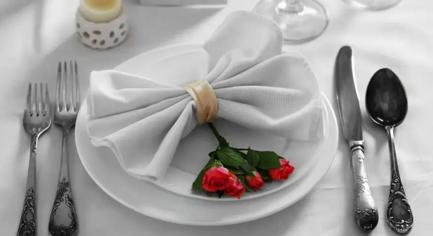 Mesa elegante: tenedor a la izquierda, cuchillo y cuchara a la derecha. Servilleta con rosas, ideal para saber como colocar los cubiertos en la mesa.