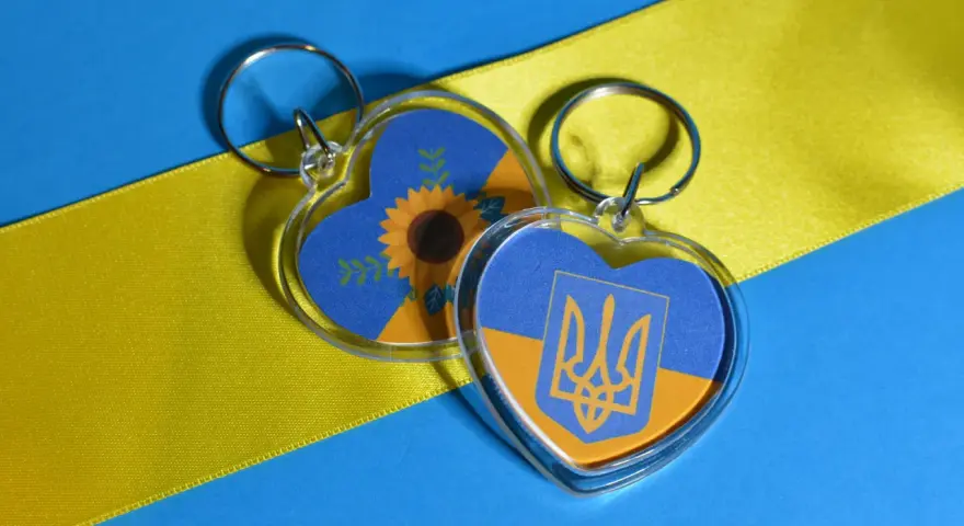 Dos llaveros en forma de corazón con la bandera de Ucrania. Uno tiene un girasol, el otro el escudo. Ideas para como hacer llaveros personalizados.