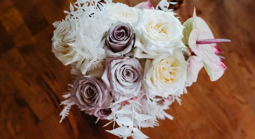 Un ramo de novia con rosas blancas y lilas, helechos blancos y una flor de anthurium rosa. Un recuerdo para secar y atesorar.