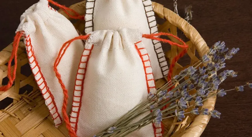 Bolsitas perfumadas para armarios caseras, hechas a mano con tela de lino y cordones rojos, junto a un manojo de lavanda seca en una cesta de mimbre.