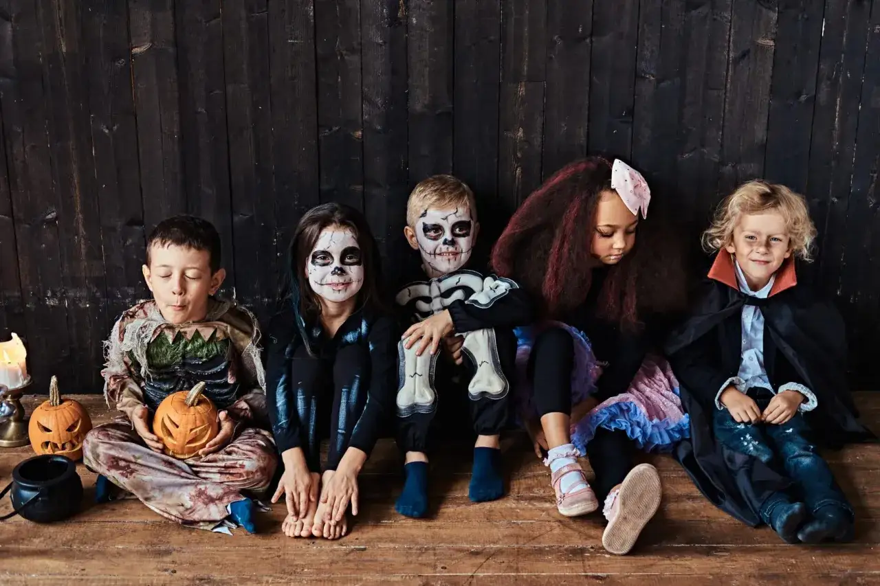 Cinco ni&ntilde;os sentados, listos para Halloween. Uno con un disfraz de juguete casero de zombi, otro de esqueleto, y un peque&ntilde;o vampiro.