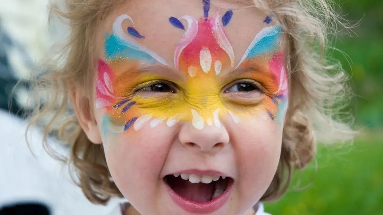 Niña con cara pintada de colores vibrantes, lista para el carnaval. Su sonrisa contagiosa y el maquillaje festivo la hacen lucir como una pequeña mariposa.