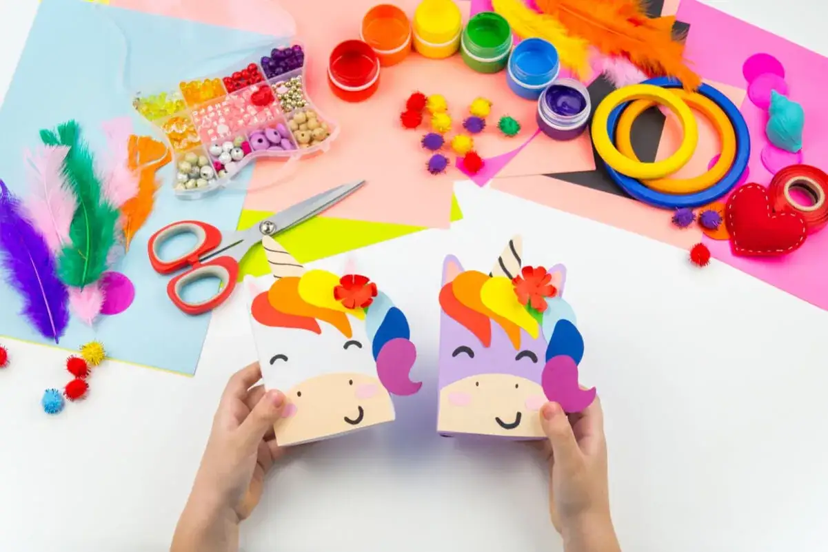 Manos infantiles crean unicornios coloridos con materiales para una fiesta barata y original.