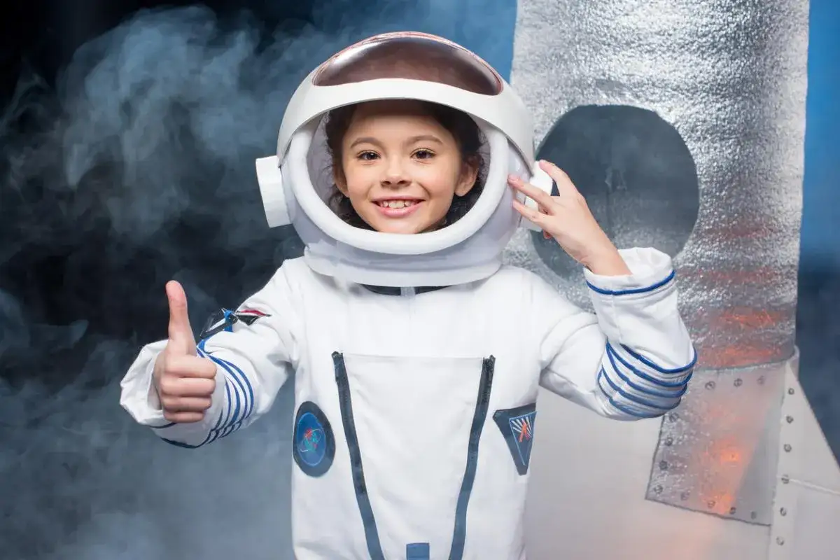 Ni&ntilde;a sonriente con un disfraz astronauta casero, pulgar arriba, lista para despegar en su cohete espacial.