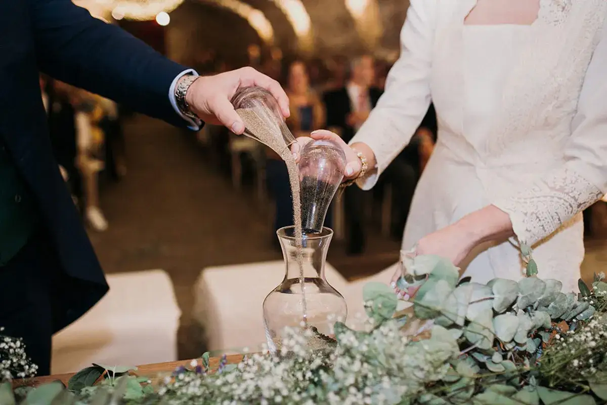Manos de novios vierten arena en un jarrón, simbolizando el ritual de la arena boda. Sus vidas se unen, como la arena que se mezcla.