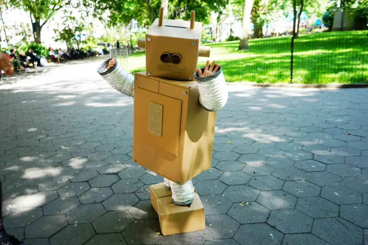 Un ni&ntilde;o saluda con su disfraz robot casero hecho de cart&oacute;n, con brazos y piernas flexibles, listo para explorar el parque.