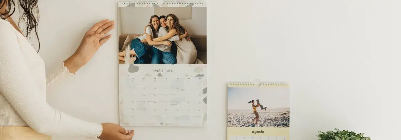 Un calendario personalizado con fotos de amigos y familia. Un mes muestra a tres amigas abrazándose, otro a una madre jugando con su hijo en la playa.