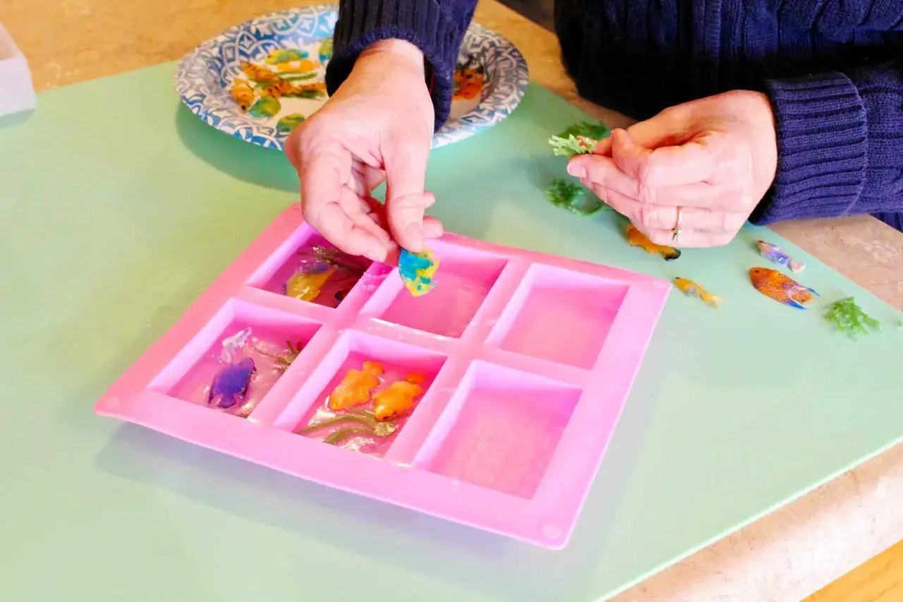 Manos colocando peces de colores en moldes para hacer jabones para ni&ntilde;os.