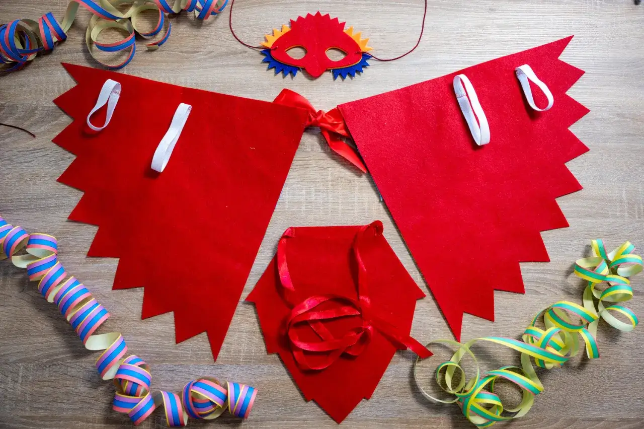 M&aacute;scara y capa de fieltro rojo para un disfraz p&aacute;jaro casero, junto a serpentinas de fiesta.