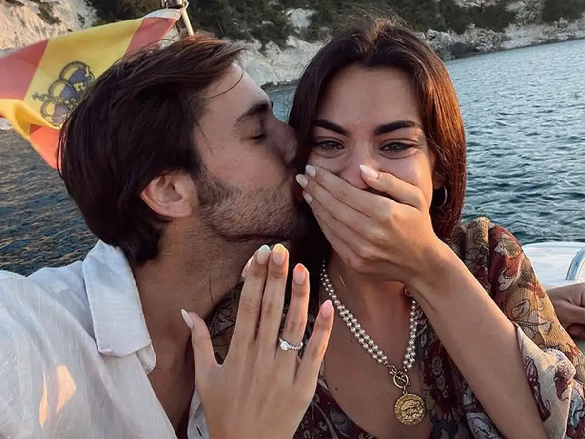 Un hombre besa a una mujer en el mar, ella muestra un anillo de compromiso. Una pedida de mano original con la bandera espa&ntilde;ola de fondo.