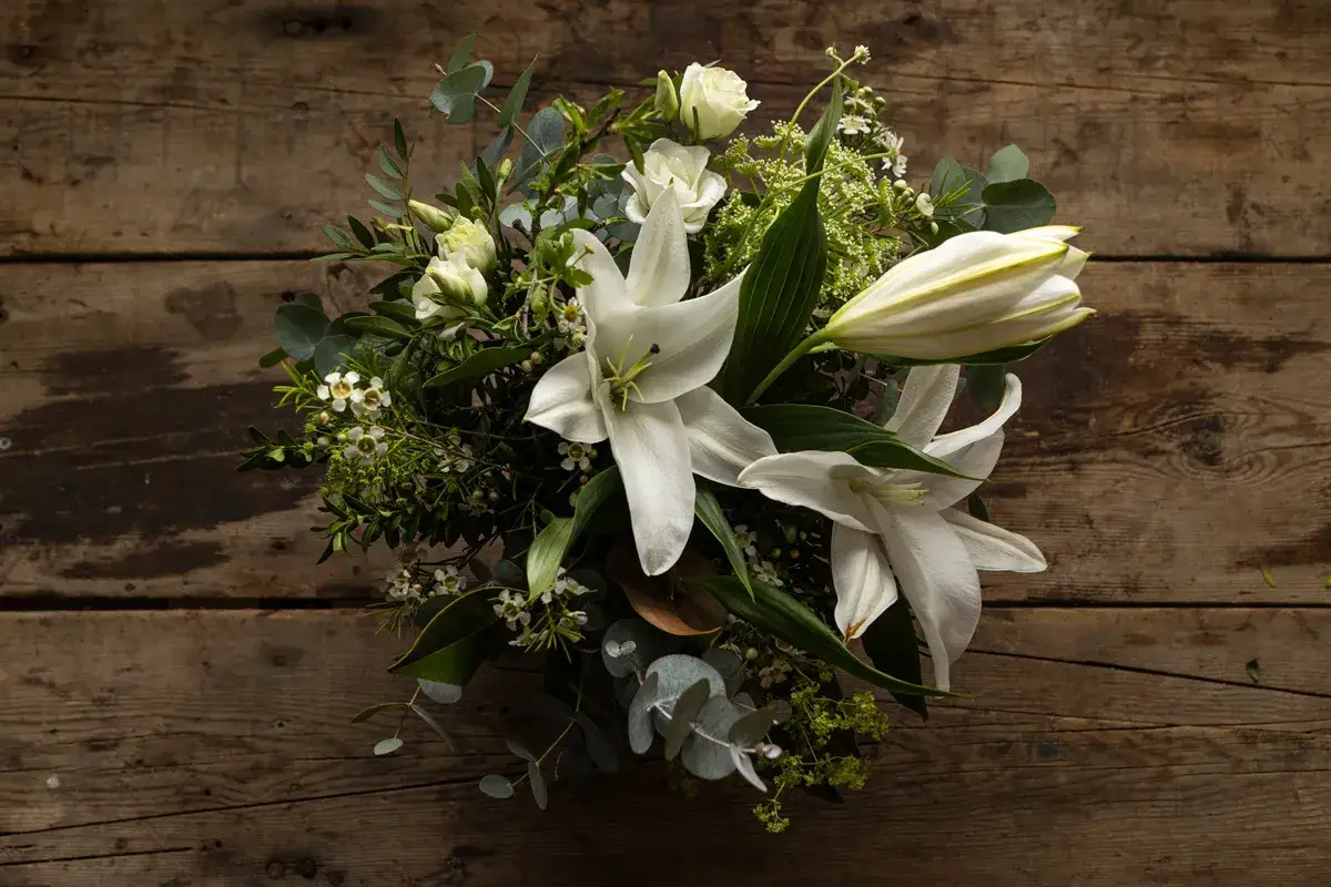 Un ramo de novia con lirios blancos y rosas sobre madera rústica. Un recuerdo para secar y atesorar.