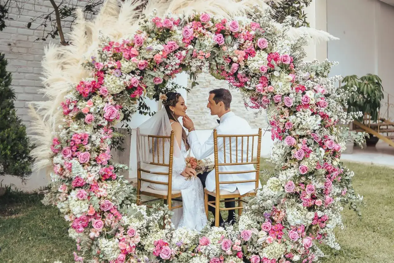 Novios bajo un arco floral rosa y blanco. Una decoraci&oacute;n boda civil sencilla y barata que crea un ambiente rom&aacute;ntico y natural.