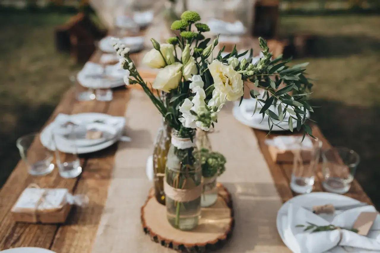 Arreglo floral r&uacute;stico en botellas recicladas sobre mesa de madera, perfecto para una boda barata y encantadora.