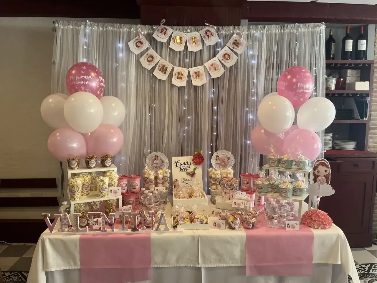 Mesa de dulces para Primera Comunión con globos rosas y blancos, banderines y detalles de chuches. ¡Ideas originales con chuches para celebrar!