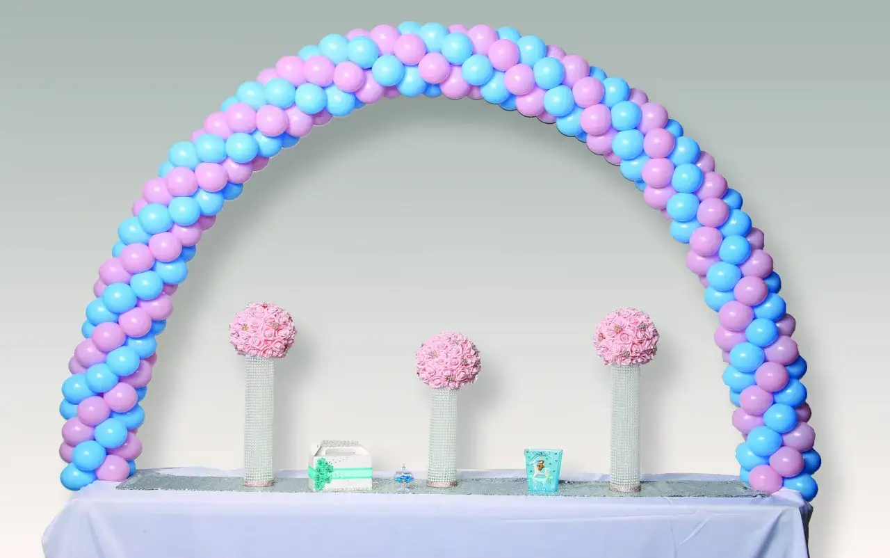 Arco de globos rosa y azul, perfecto para un feliz cumpleaños. Tres centros de mesa con flores rosas y detalles brillantes.