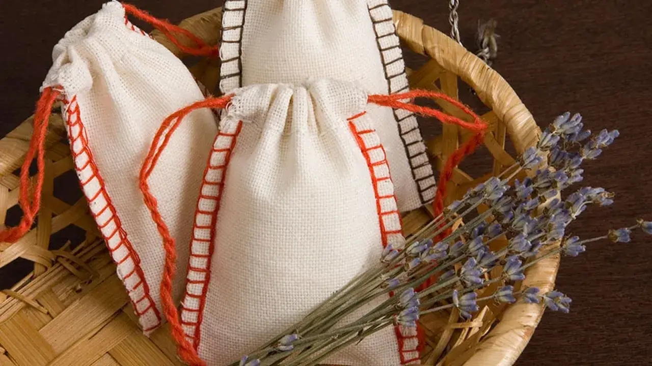 Bolsitas perfumadas para armarios caseras, hechas a mano con tela de lino y cordones rojos, junto a un manojo de lavanda seca en una cesta de mimbre.