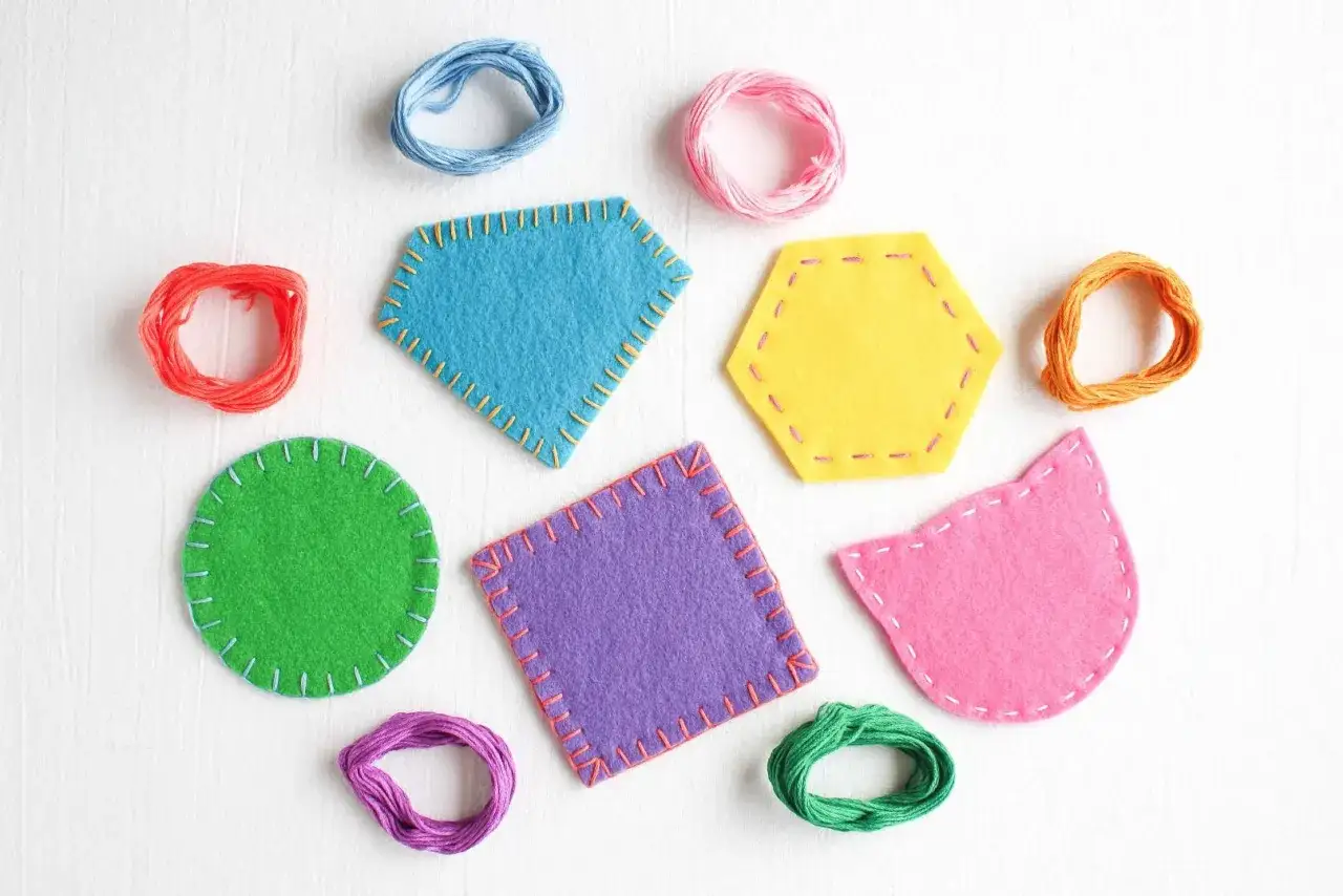 Posavasos de fieltro de colores, con formas geométricas y de gato, rodeados de hilos para coser.