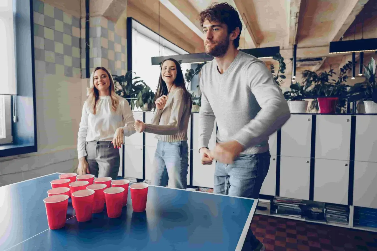 J&oacute;venes riendo y jugando beer pong, perfectos juegos para comida de empresa.