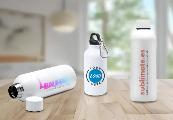 Tres bidones personalizados en una mesa de madera. Uno con logo "BAUHAUS", otro con "YOUR LOGO HERE" y el tercero con "sublimate.es".