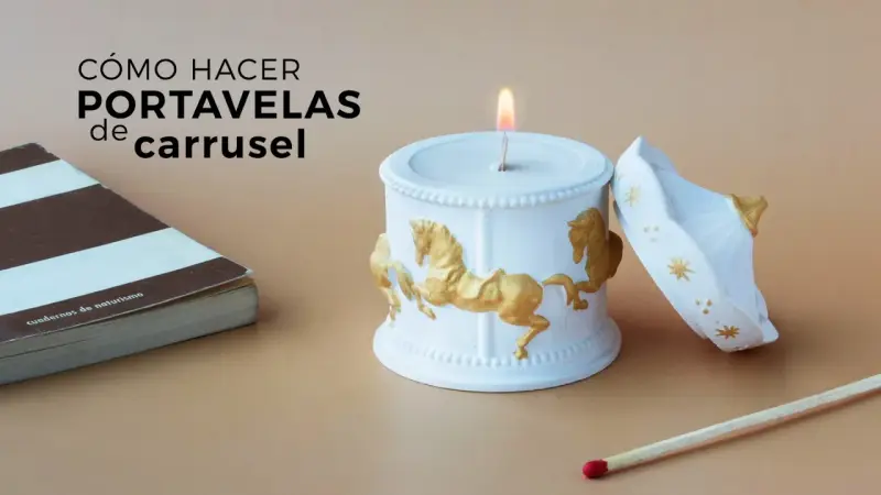 Portavelas manualidades de carrusel, blanco con caballos dorados, junto a un libro y una cerilla.